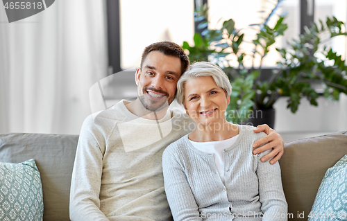 Image of senior mother with adult son hugging at home