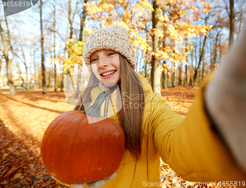 Image of girl with pumpkin taking selfie at autumn park