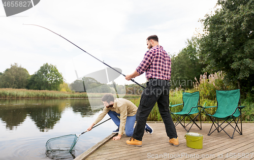 Image of male friends with net and fishing rods on lake