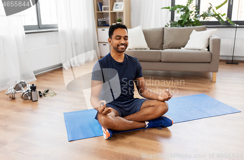 Image of indian man meditating in lotus pose at home