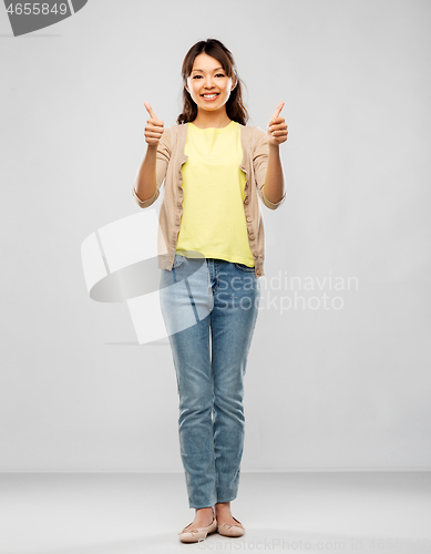 Image of happy asian woman showing thumbs up over grey