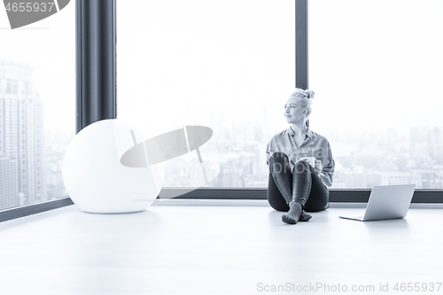 Image of woman drinking coffee and using laptop at home