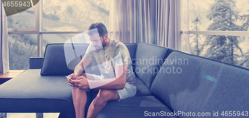 Image of young casual man using a mobile phone at home