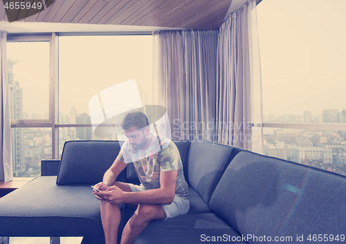 Image of young casual man using a mobile phone at home