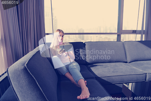 Image of young woman on sofa at home surfing web