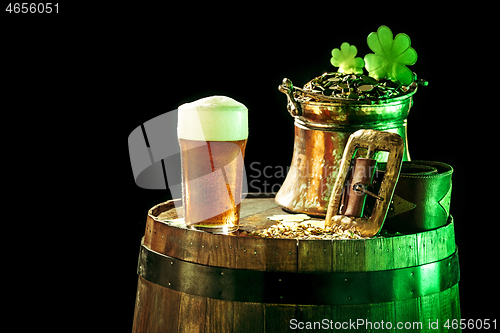 Image of The wooden background with lots of gold coins and a large mug of beer with a green bow.