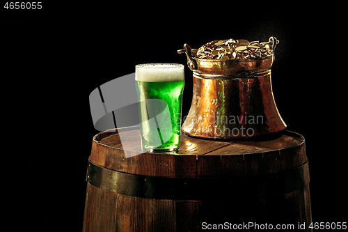 Image of The wooden background with lots of gold coins and a large mug of beer with a green bow.