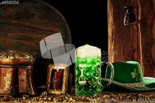 Image of The wooden background with lots of gold coins and a large mug of beer with a green bow.