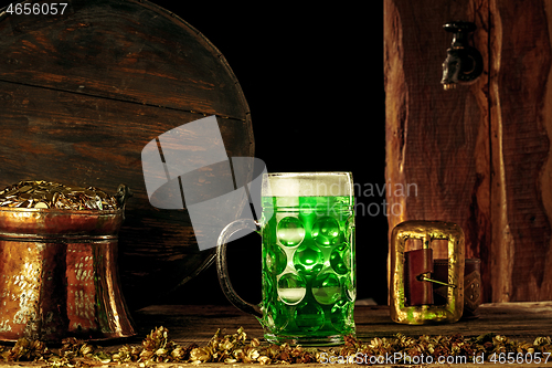 Image of The wooden background with lots of gold coins and a large mug of beer with a green bow.