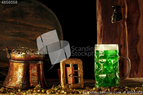 Image of The wooden background with lots of gold coins and a large mug of beer with a green bow.