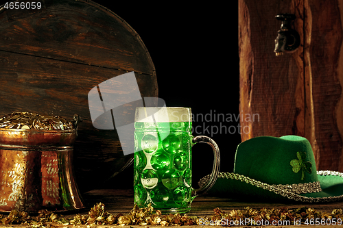 Image of The wooden background with lots of gold coins and a large mug of beer with a green bow.