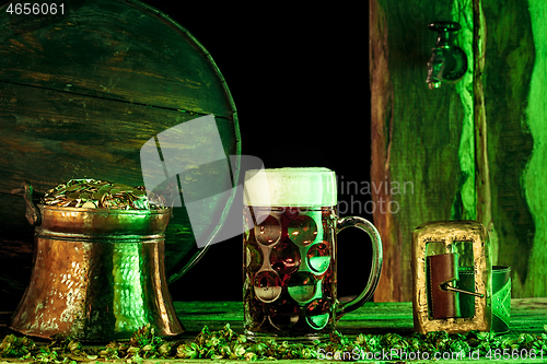 Image of The wooden background with lots of gold coins and a large mug of beer with a green bow.