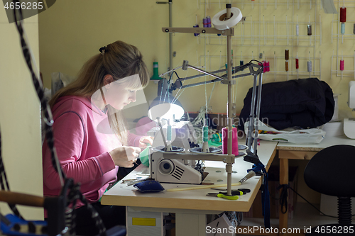 Image of Fashion designer clothes sews on sewing machine by light lamp in workshop