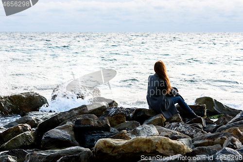 Image of A girl sits on stony stones by the sea and looks into the distance