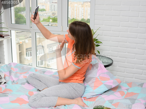 Image of Girl sitting on bed at home happily communicates with her friend via video calling