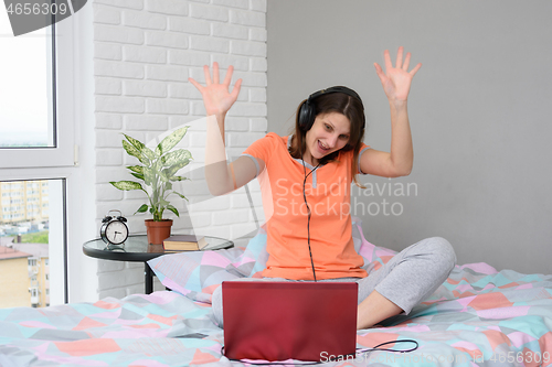 Image of The girl is funny and welcoming waving her hands while looking at the laptop screen