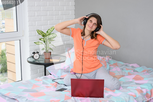 Image of The girl put on her headphones, connected them to the computer and is listening to music happily