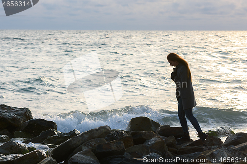 Image of Lonely girl in a depressed mood walking along a rocky seashore
