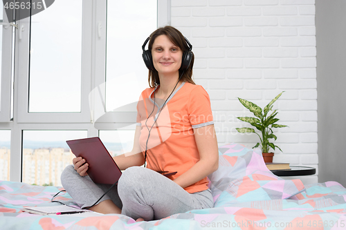Image of Girl in headphones and with a laptop sits at home in bed, dressed in pajamas