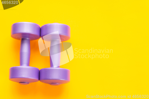 Image of Two purple dumbbells lie next to a yellow background