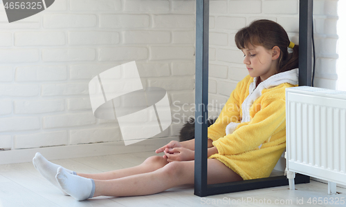 Image of Sad girl sits on the floor under the table, cat sleeps nearby