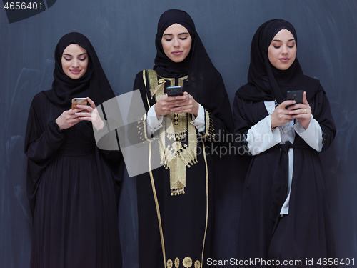 Image of muslim women using mobile phone in front of black chalkboard