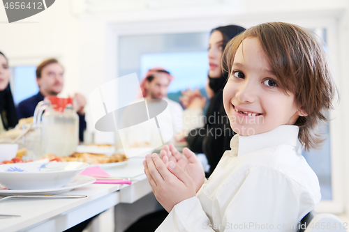 Image of little muslim boy praying with family before iftar dinner