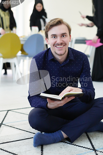 Image of young muslim man reading Quran at home