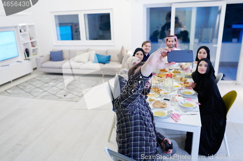 Image of Muslim family having Iftar dinner taking pictures with mobile ph