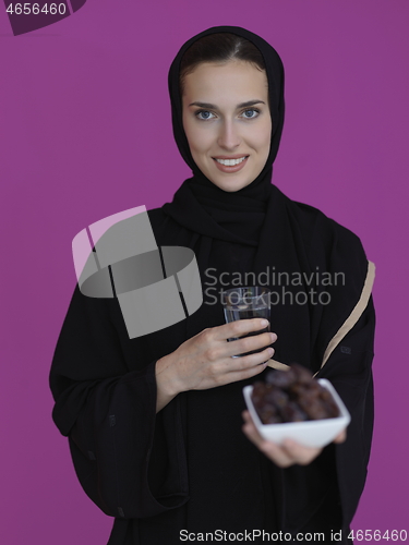 Image of Woman in Abaya Holding a Date Fruit and glass of water