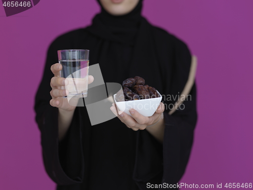 Image of Woman in Abaya Holding a Date Fruit and glass of water