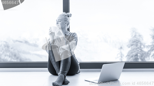 Image of woman drinking coffee and using laptop at home