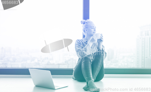 Image of woman drinking coffee and using laptop at home