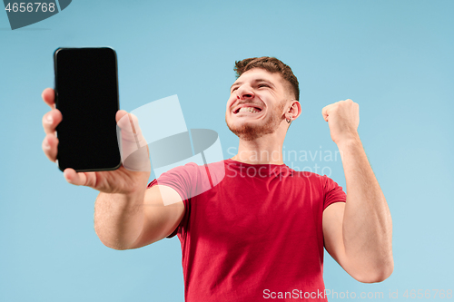 Image of Young handsome man showing smartphone screen isolated on blue background in shock with a surprise face