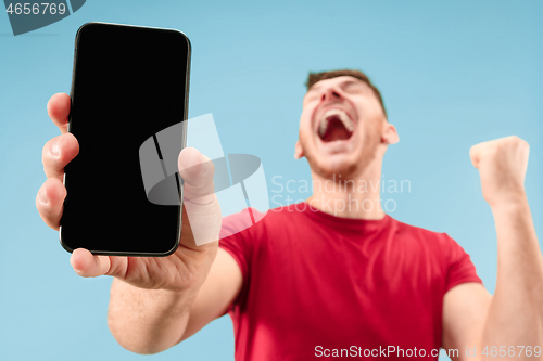 Image of Young handsome man showing smartphone screen isolated on blue background in shock with a surprise face