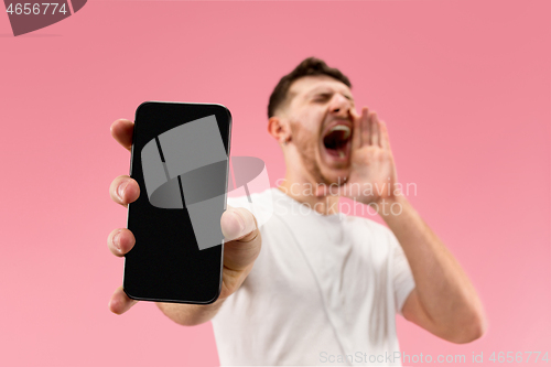 Image of Young handsome man showing smartphone screen isolated on pink background in shock with a surprise face