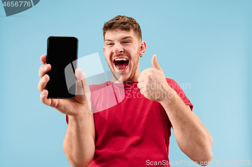Image of Young handsome man showing smartphone screen isolated on blue background in shock with a surprise face