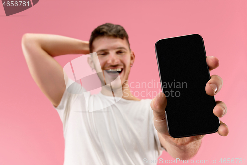 Image of Young handsome man showing smartphone screen isolated on pink background in shock with a surprise face