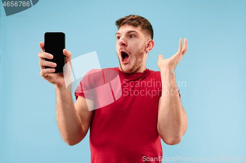 Image of Young handsome man showing smartphone screen isolated on blue background in shock with a surprise face