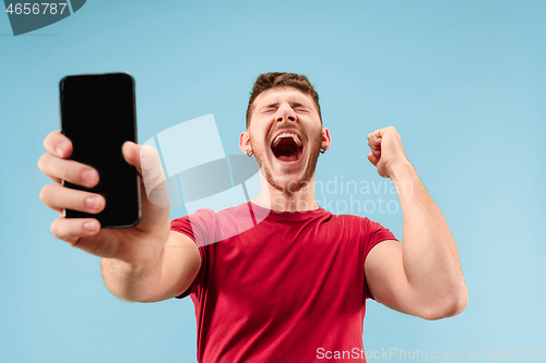 Image of Young handsome man showing smartphone screen isolated on blue background in shock with a surprise face