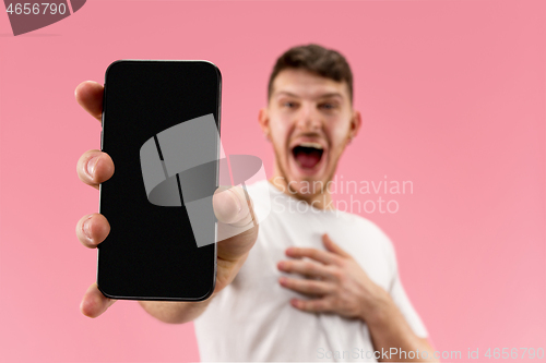 Image of Young handsome man showing smartphone screen isolated on pink background in shock with a surprise face