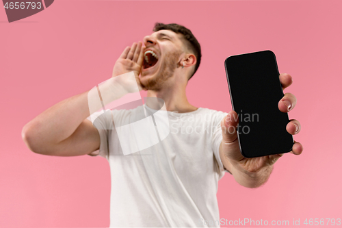 Image of Young handsome man showing smartphone screen isolated on pink background in shock with a surprise face
