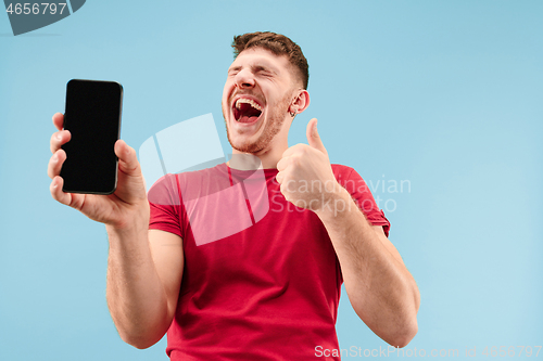 Image of Young handsome man showing smartphone screen isolated on blue background in shock with a surprise face