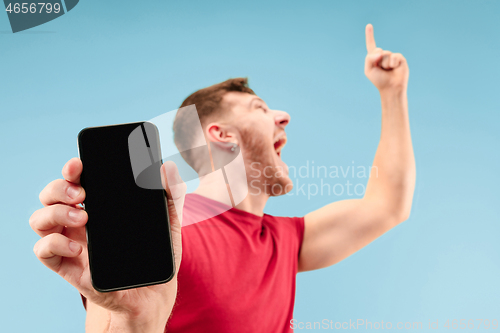 Image of Young handsome man showing smartphone screen isolated on blue background in shock with a surprise face