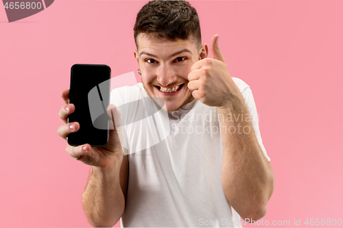 Image of Young handsome man showing smartphone screen isolated on pink background in shock with a surprise face