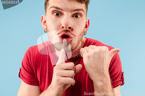 Image of The young man whispering a secret behind her hand over blue background