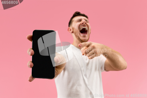 Image of Young handsome man showing smartphone screen isolated on pink background in shock with a surprise face