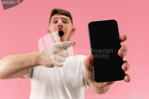 Image of Young handsome man showing smartphone screen isolated on pink background in shock with a surprise face