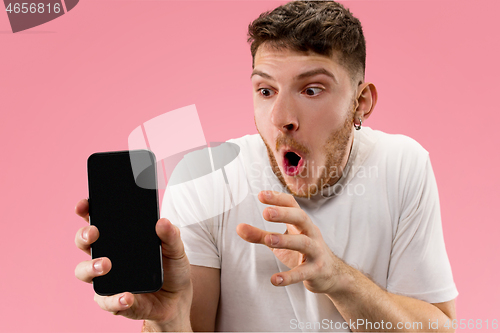 Image of Young handsome man showing smartphone screen isolated on pink background in shock with a surprise face