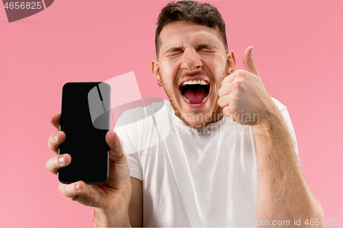 Image of Young handsome man showing smartphone screen isolated on pink background in shock with a surprise face